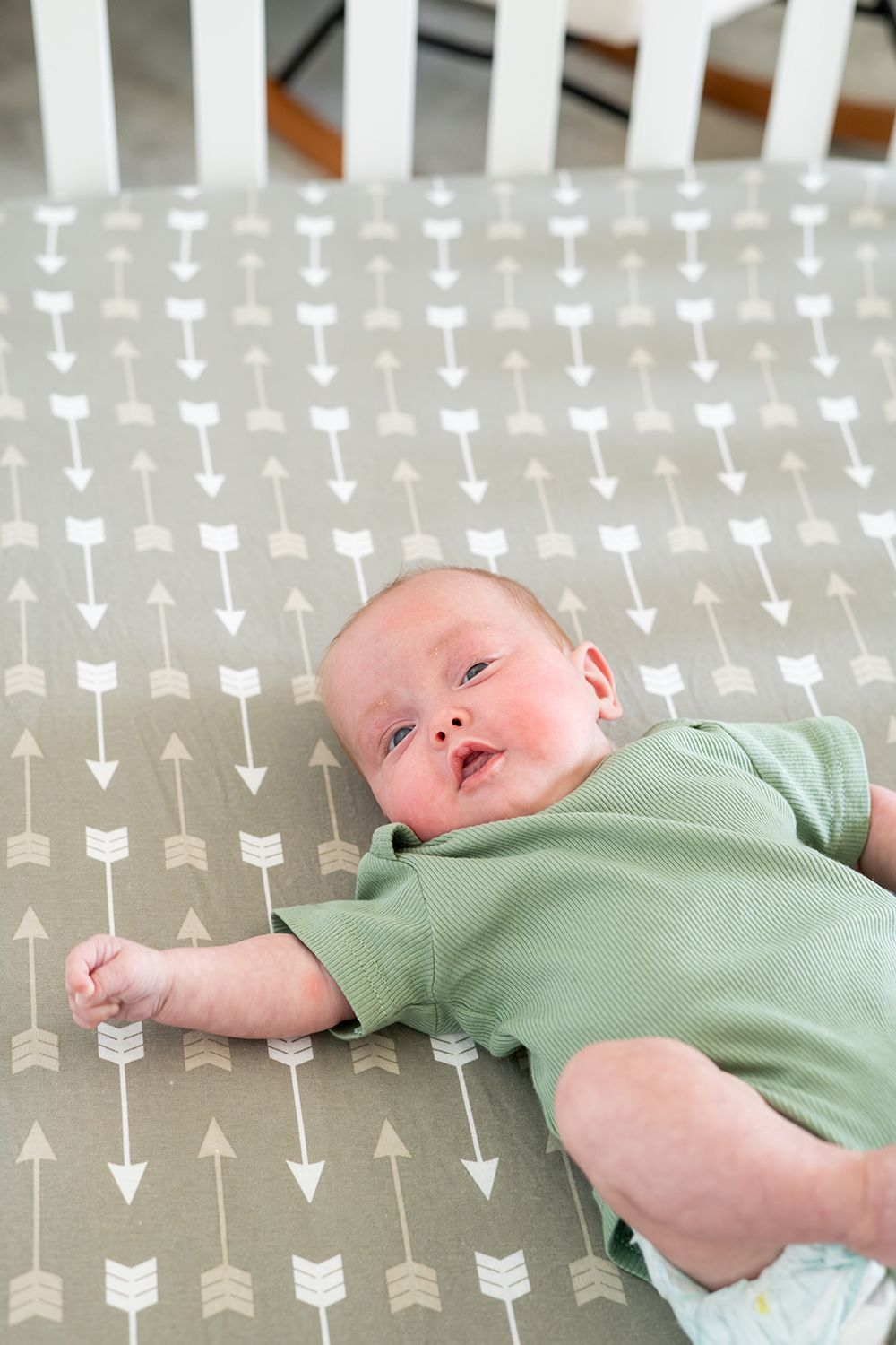 A baby wearing a mint green outfit rests on a gray and white arrow patterned blanket.