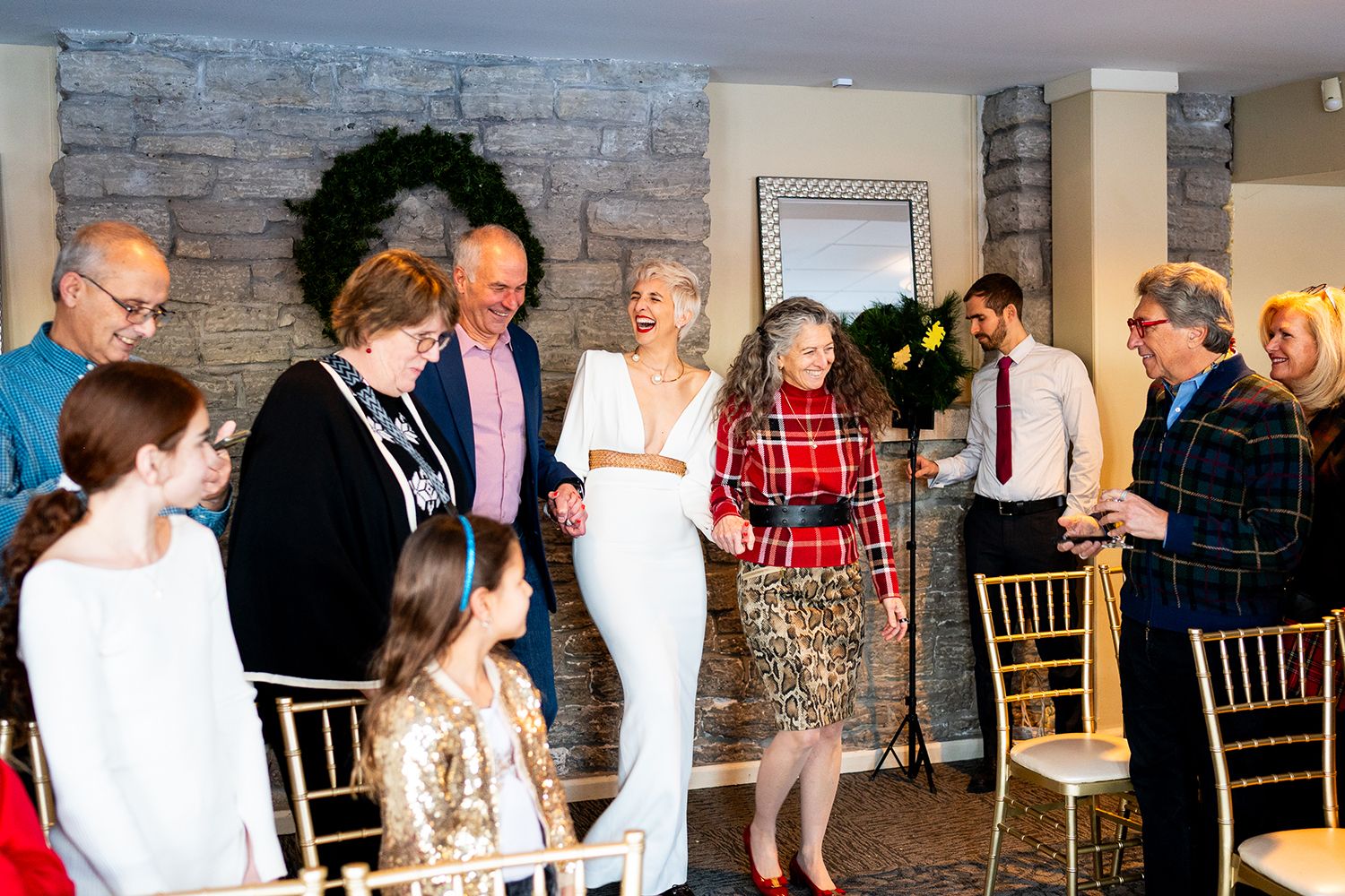 Group of wedding guests enjoying conversation and refreshments at a reception with stone wall decor in background.