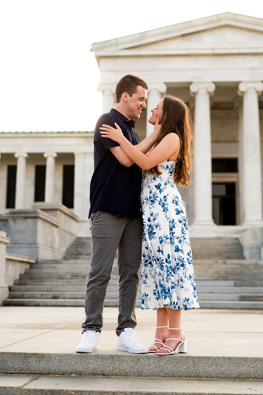 A couple embraces on stone steps in front of a neoclassical building with white columns during a romantic moment.