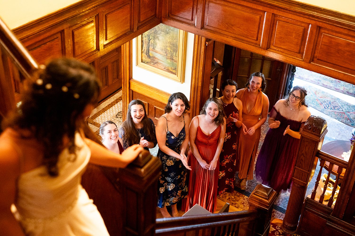 A wedding party gathering on an elegant wooden staircase with warm lighting and decorative wood paneling.