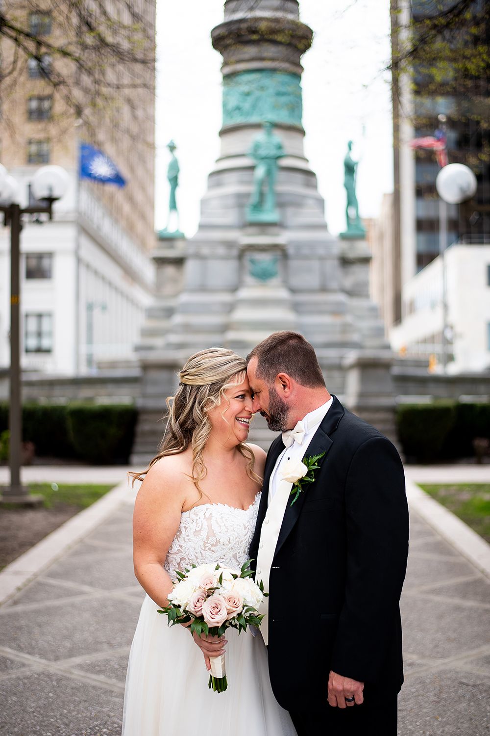 Romantic wedding couple embraces in front of historic architecture with ornate columns and patina details.