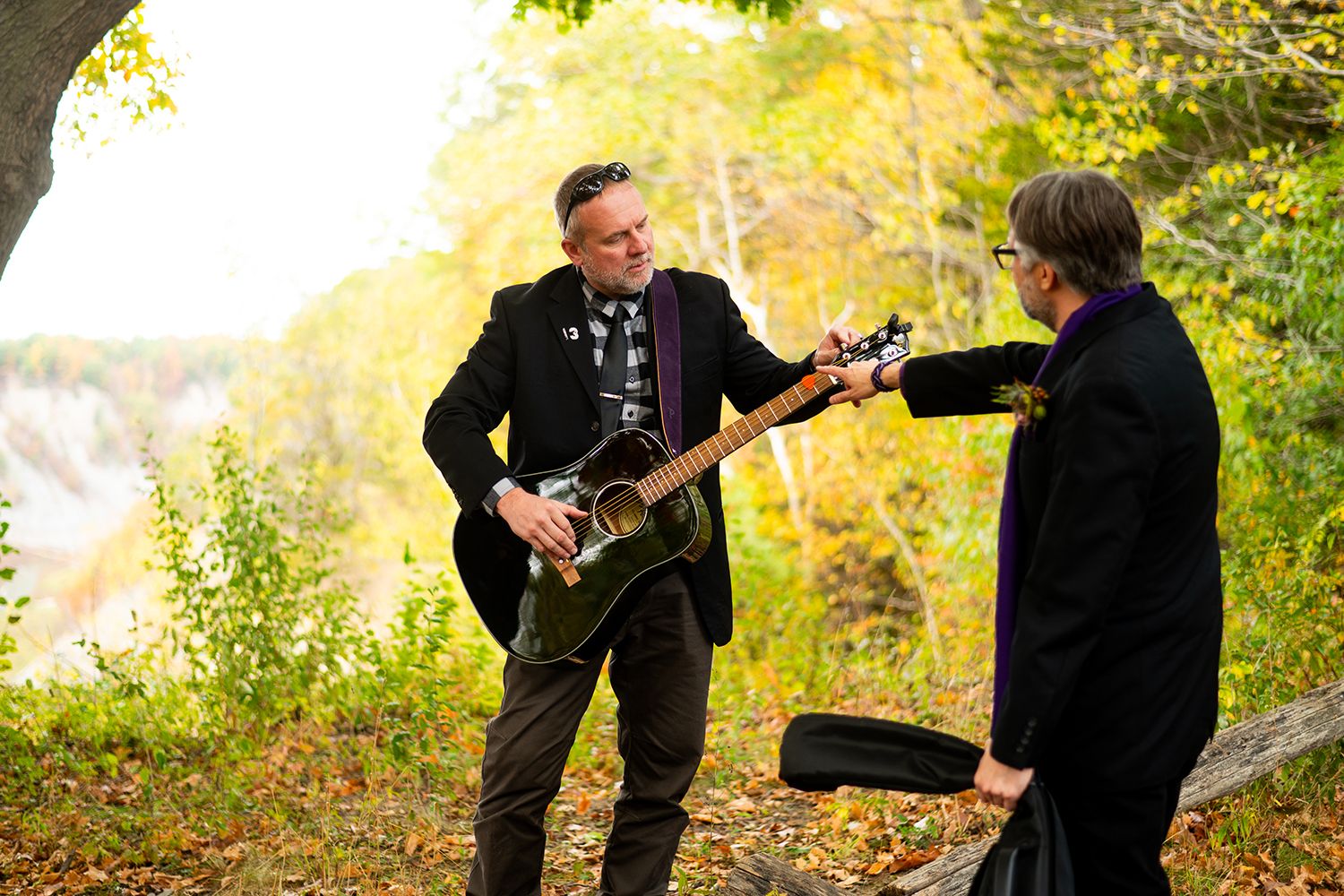 Two figures dressed in dark suits dance playfully together in a beautiful autumn garden setting.