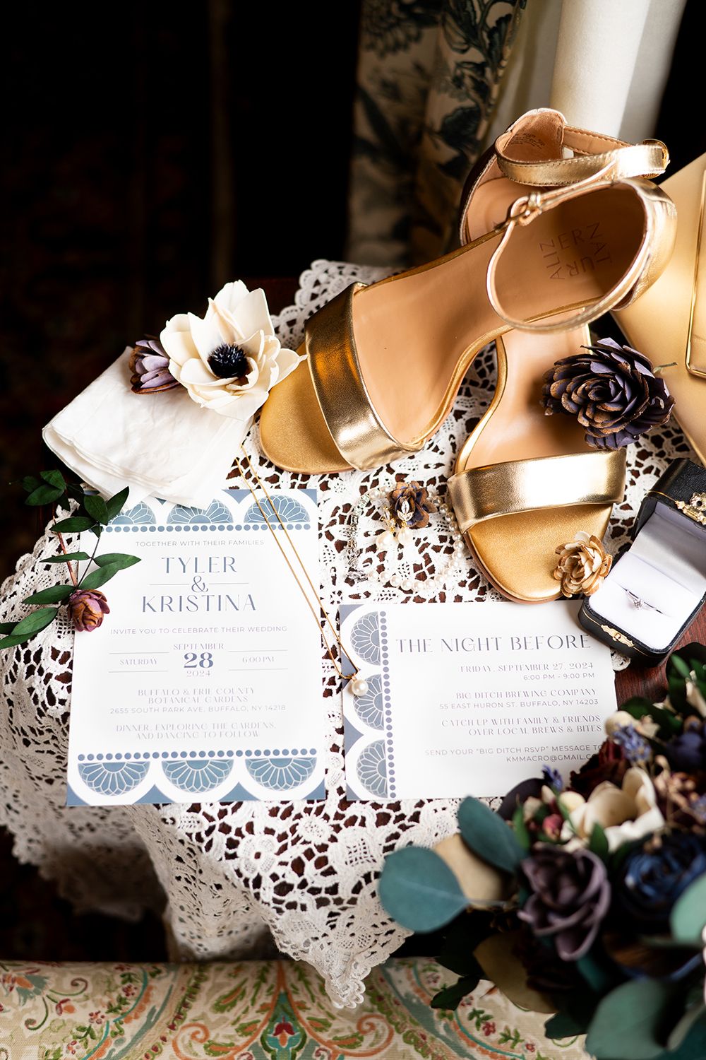 Wedding invitations and elegant beige heels arranged with delicate lace doilies and burgundy floral accents on a textured surface.