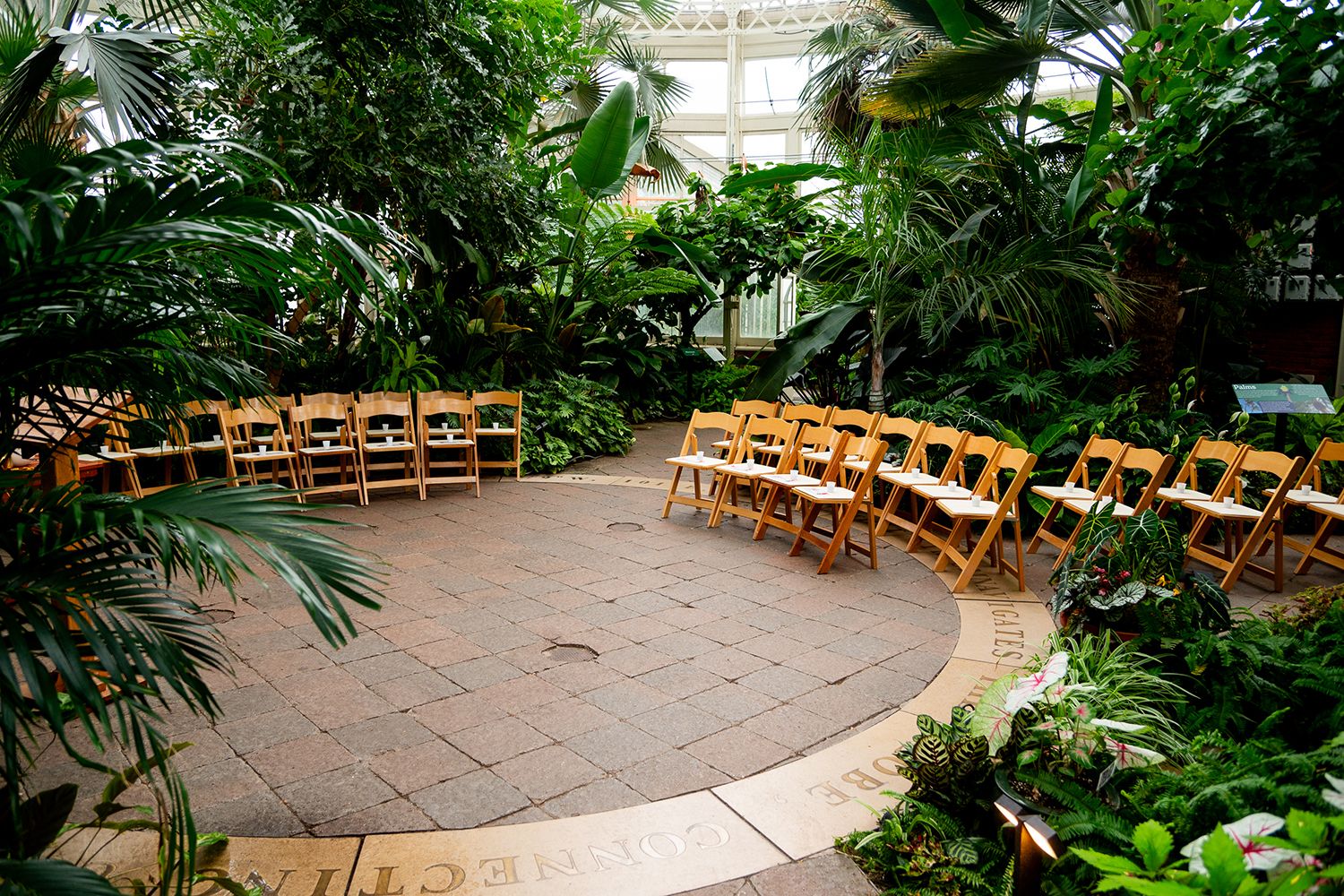 Curved stone pathway winding through a lush tropical garden with wooden chairs arranged for an outdoor ceremony.