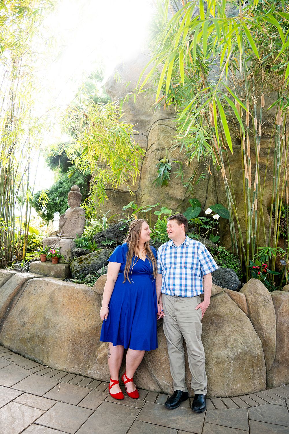 A couple stand together in a garden path surrounded by tall bamboo and rock formations.