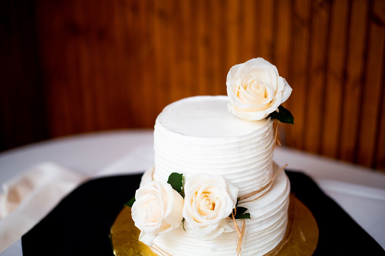 A white tiered wedding cake with delicate floral decorations displayed against a dark wooden background.