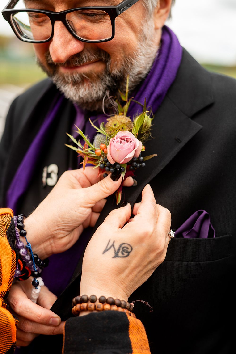 Close-up of a boutonniere being pinned to a black suit jacket with purple accents.