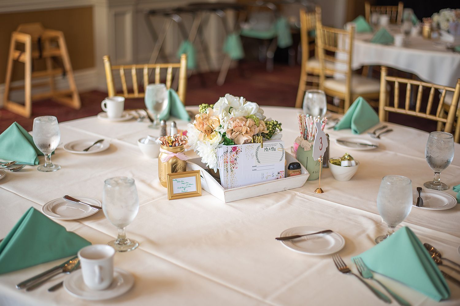Elegant wedding table setting with mint green napkins, white linens, and pastel floral centerpiece in wooden box.