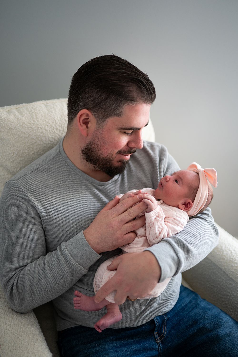 A tender moment showing an adult cradling a newborn baby in a gray sweater by a cozy white couch.