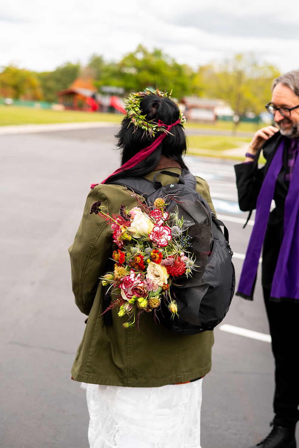 A backpack adorned with a colorful floral arrangement rests against an olive green jacket outdoors.