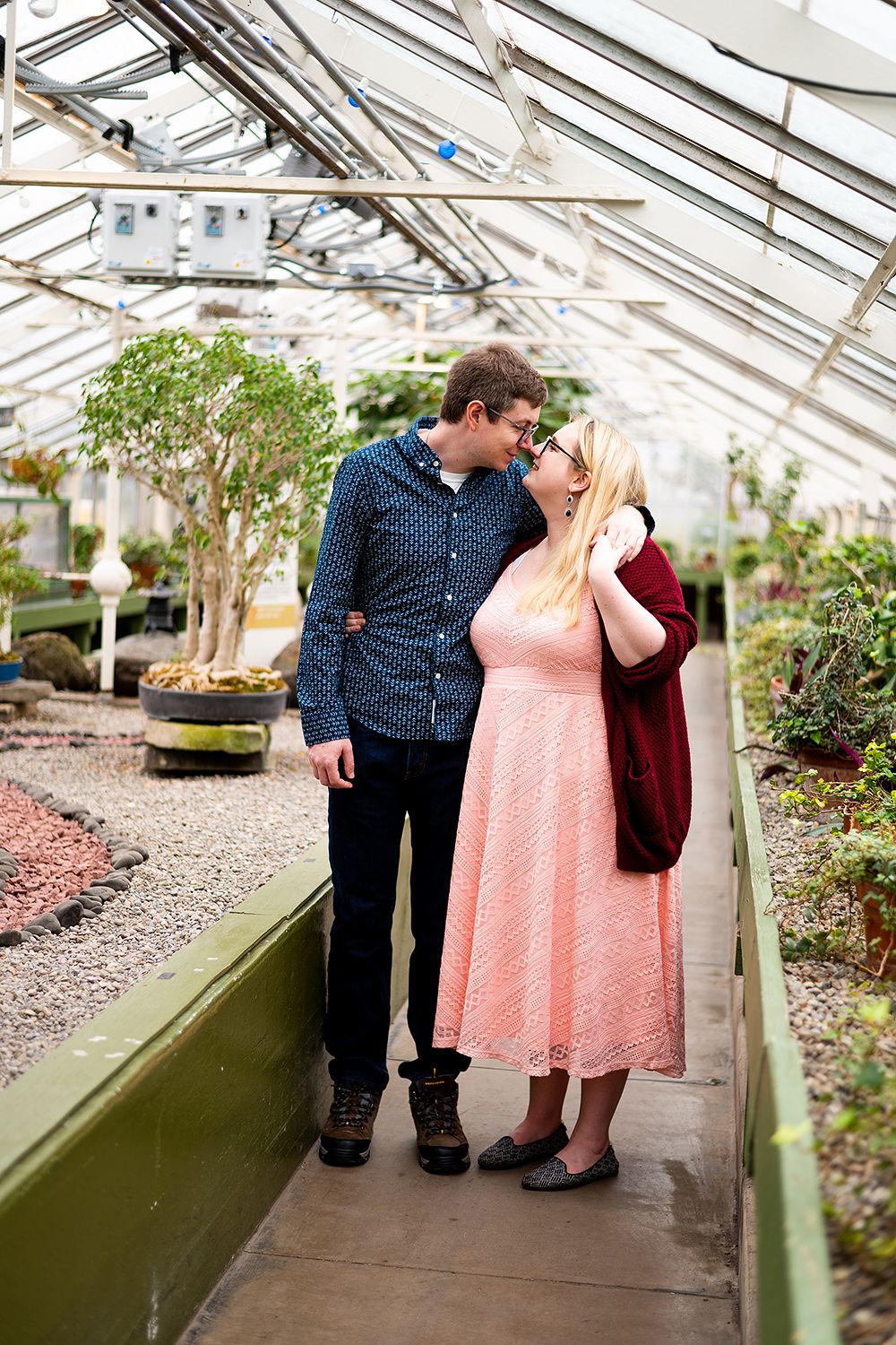 A couple sharing romantic moments in a greenhouse surrounded by plants and natural light.