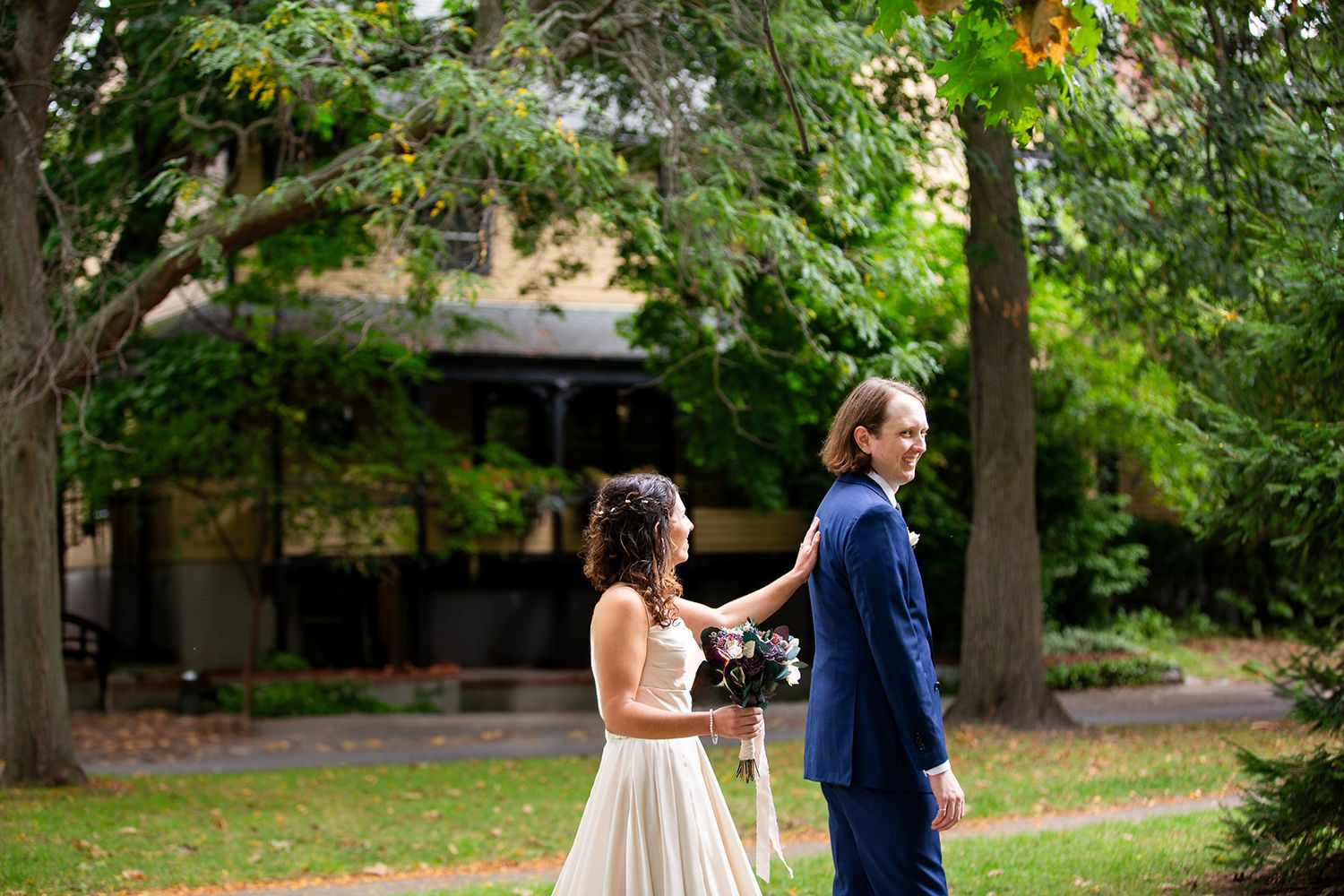 A couple in wedding attire stands together in a lush garden setting during a first look moment.