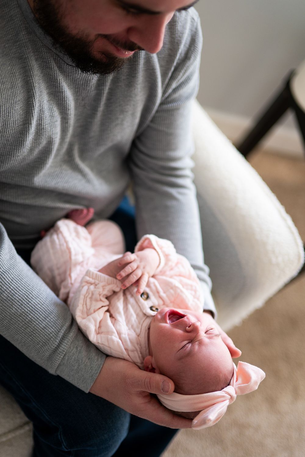 Parent in gray sweater holds a tiny baby wearing pink clothes while seated on couch.