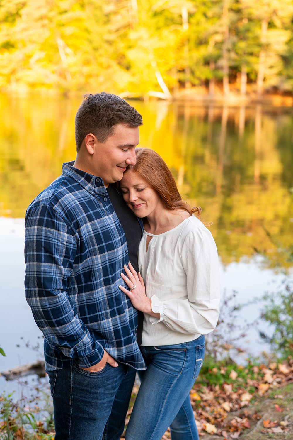 Couple sharing an intimate moment by a lake in autumn with golden foliage reflecting in the water.