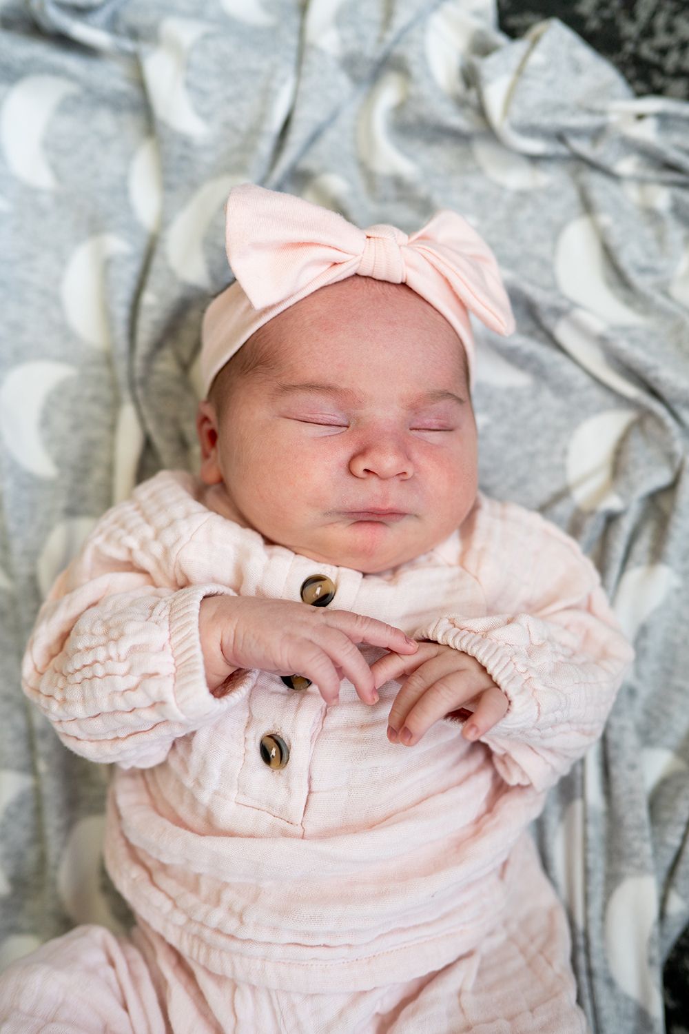 Sleeping infant in pale pink outfit rests on textured gray fabric showing different peaceful poses.