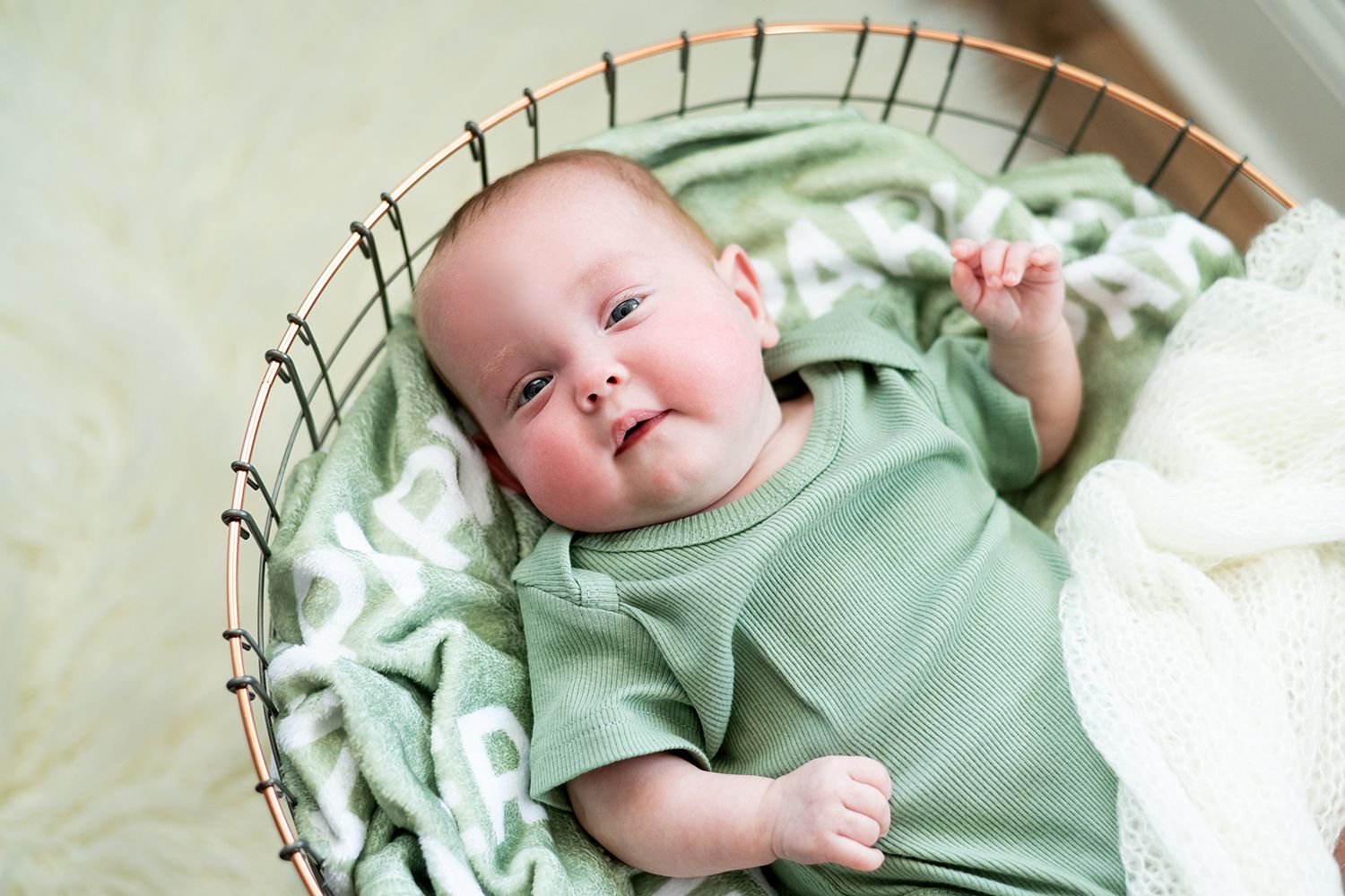 Baby wearing mint green onesie lies in a woven basket with white blankets.