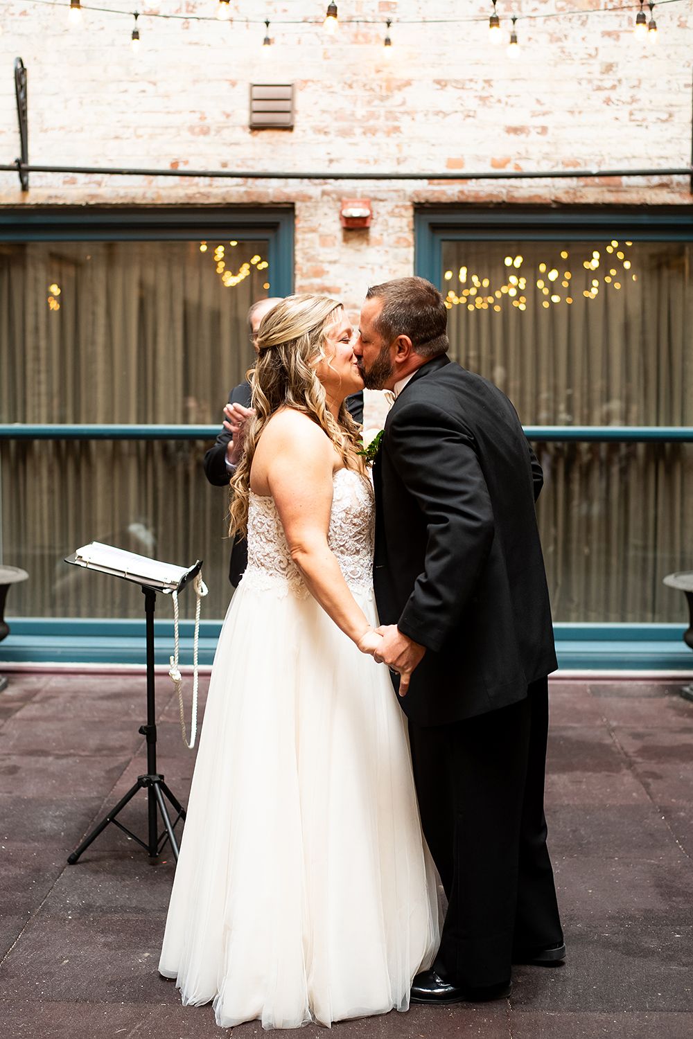 A couple shares an intimate moment during their wedding ceremony with string lights glowing in the background.