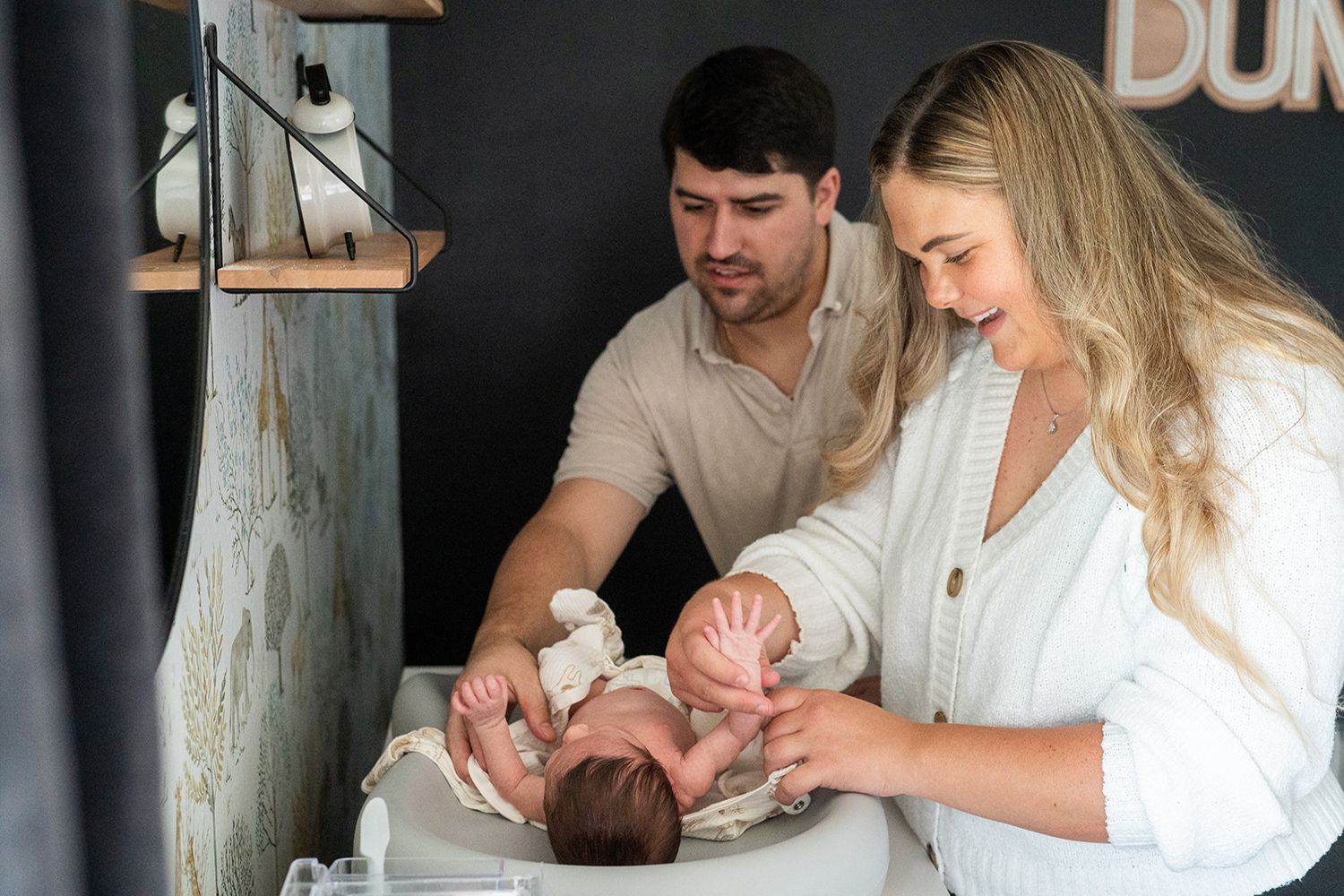 A couple changes their baby's diaper together on a changing table in a nursery setting.