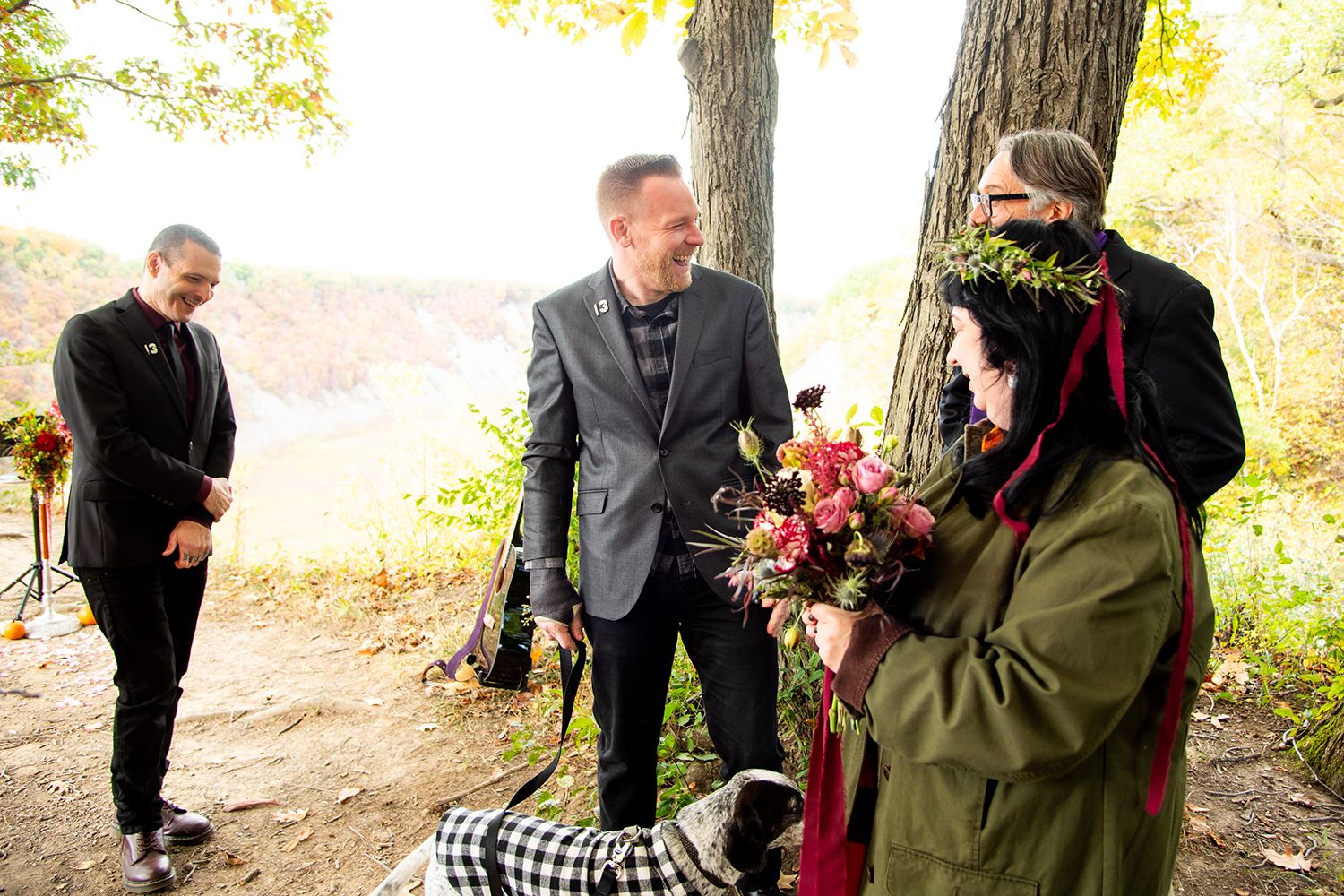 Wedding party members share candid moments on a forest trail during an autumn ceremony.
