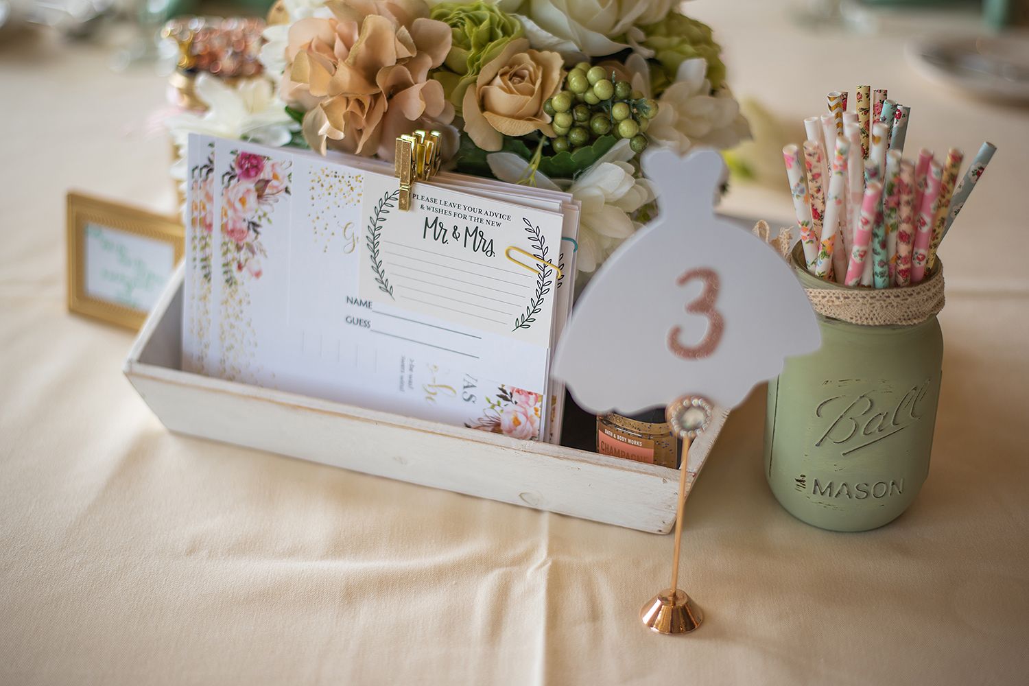 Close-up of rustic wedding table settings with vintage Mason jar centerpieces and soft peach flowers.