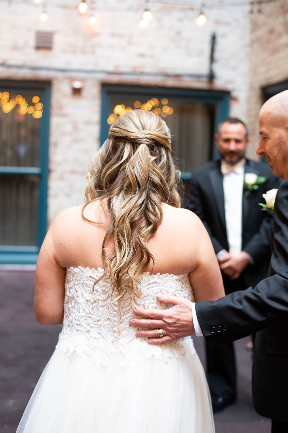 Couple shares a tender embrace at an industrial-style wedding venue with exposed brick walls and twinkling lights.