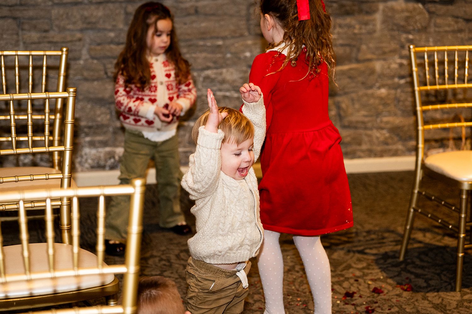 People dancing at an indoor event with gold chairs and stone walls in the background.