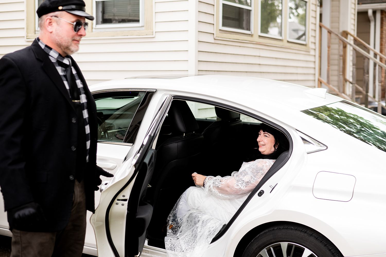 A car door is opened at a wedding showing a white lace dress inside the vehicle.