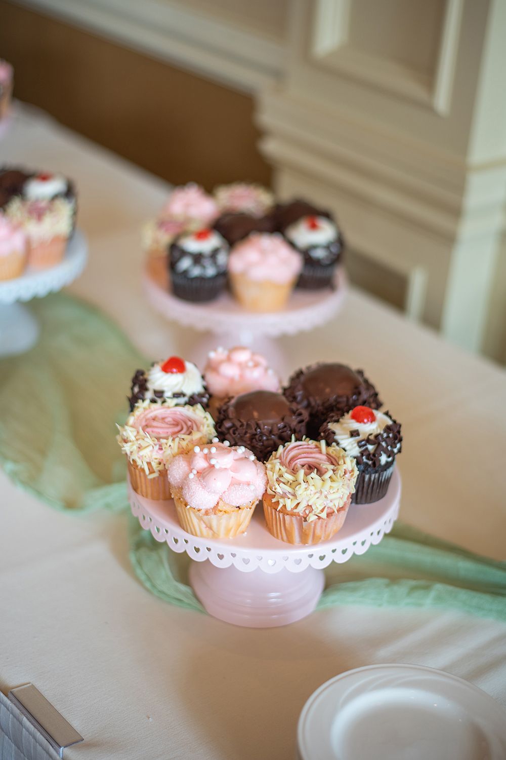 Assorted cupcakes with pink frosting and chocolate toppings displayed on a white cake stand.