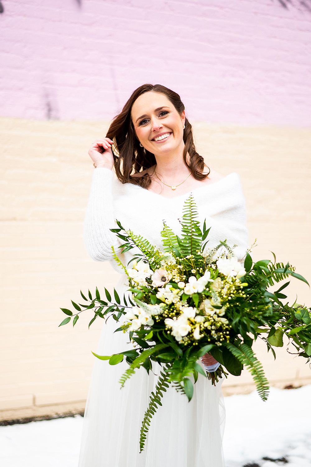 Elegant bouquet with white flowers, greenery and ferns held against a light pastel background in natural lighting.