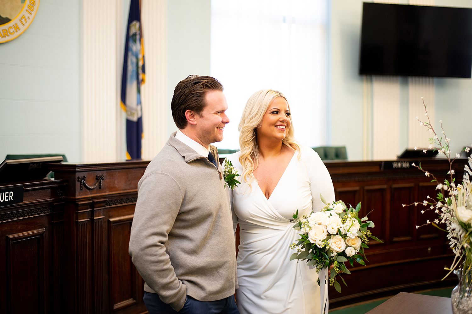 A couple shares a joyful moment during an intimate civil ceremony in a municipal building while holding white floral bouquet.