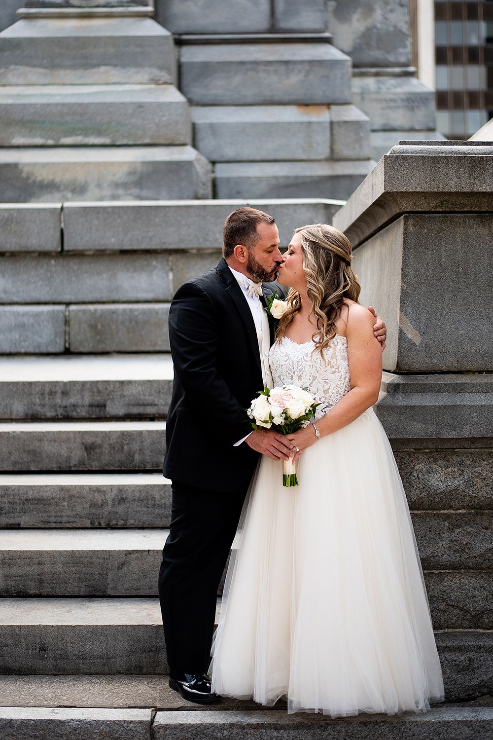 A romantic wedding moment captured on elegant stone steps with the couple sharing an intimate kiss.
