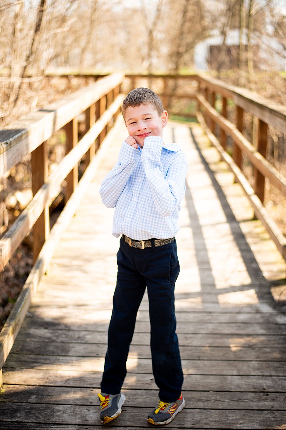 Candid outdoor portrait on wooden bridge in blue checkered shirt and navy pants.