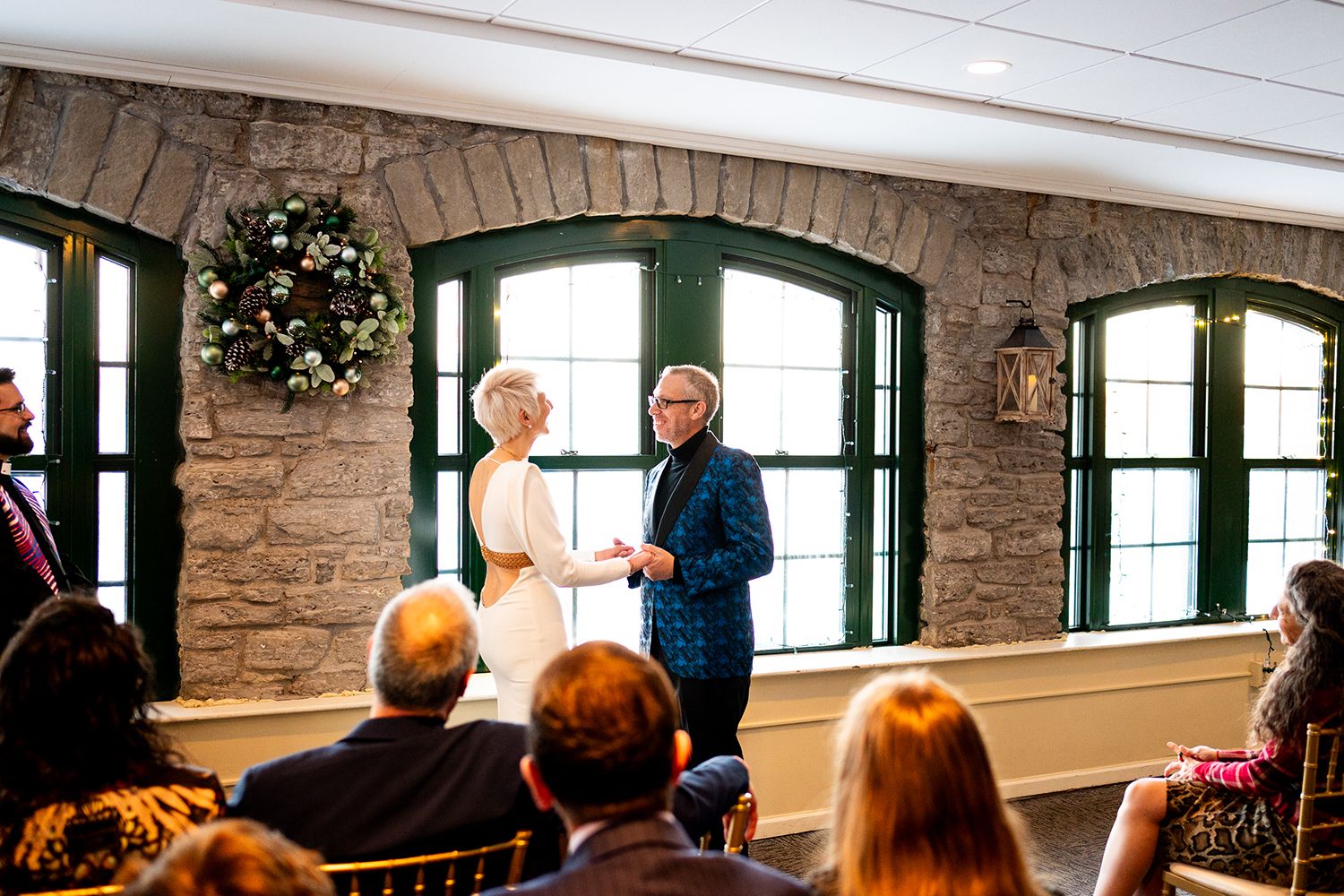 People gather in an exposed brick room with large windows and arched doorways for an indoor event.