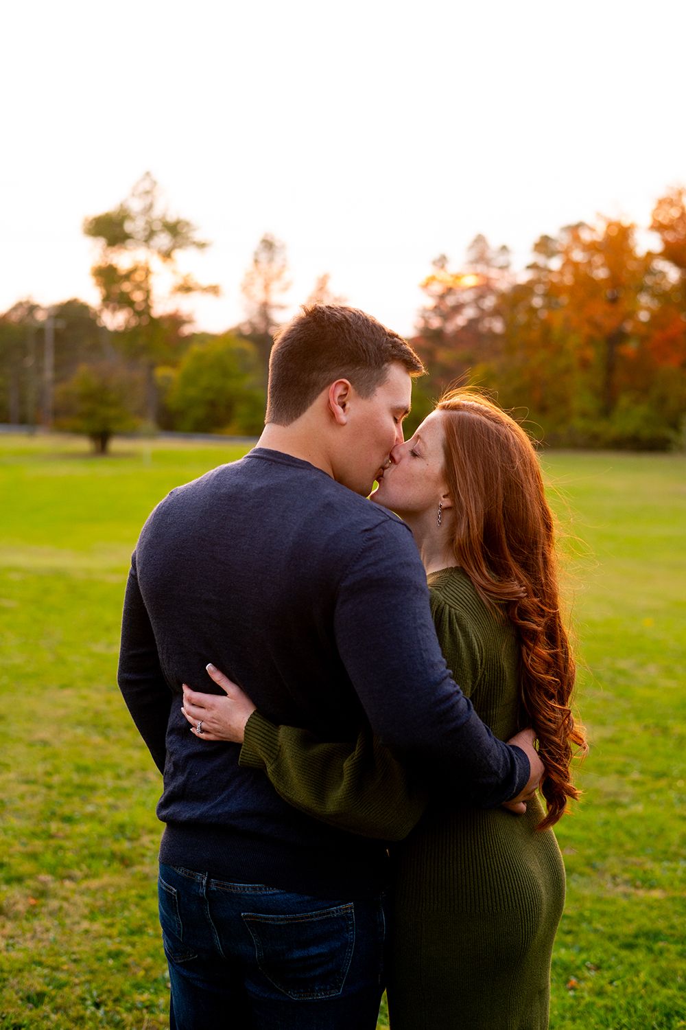 Romantic couple embracing in a green field during golden hour sunset.