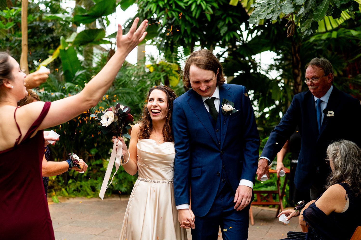 A joyous celebration in a tropical greenhouse setting with guests in formal attire.