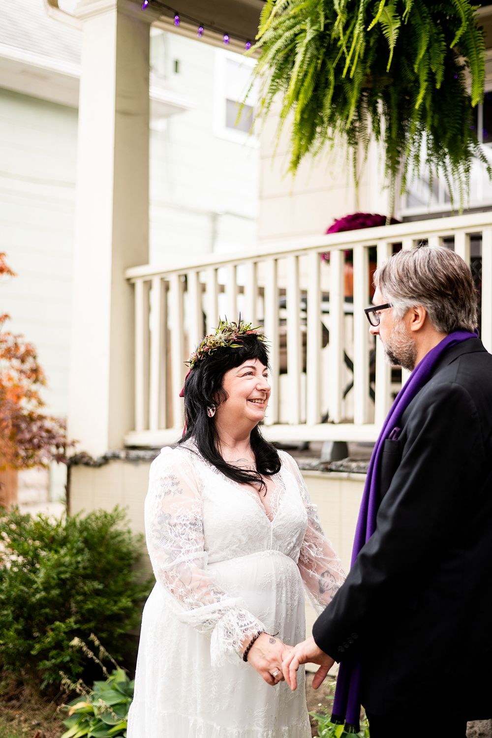 A wedding ceremony takes place on a charming white porch with hanging ferns and elegant fall decor.