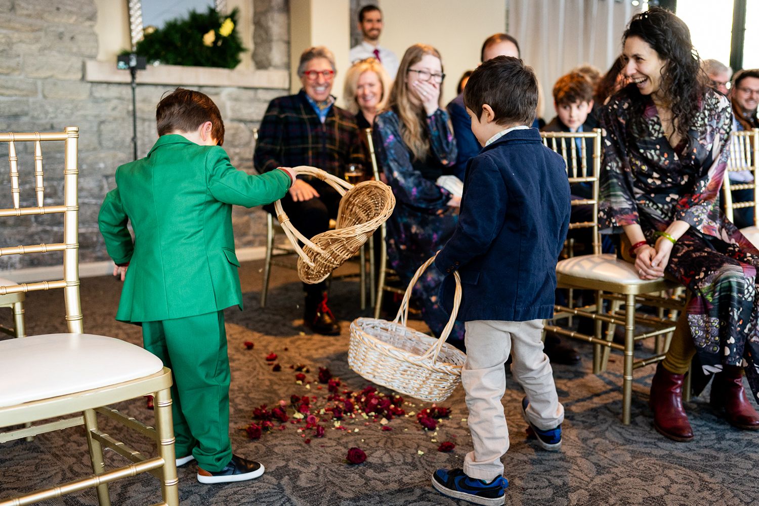 Children in matching outfits carry flower baskets along an aisle during a wedding ceremony as guests smile on.