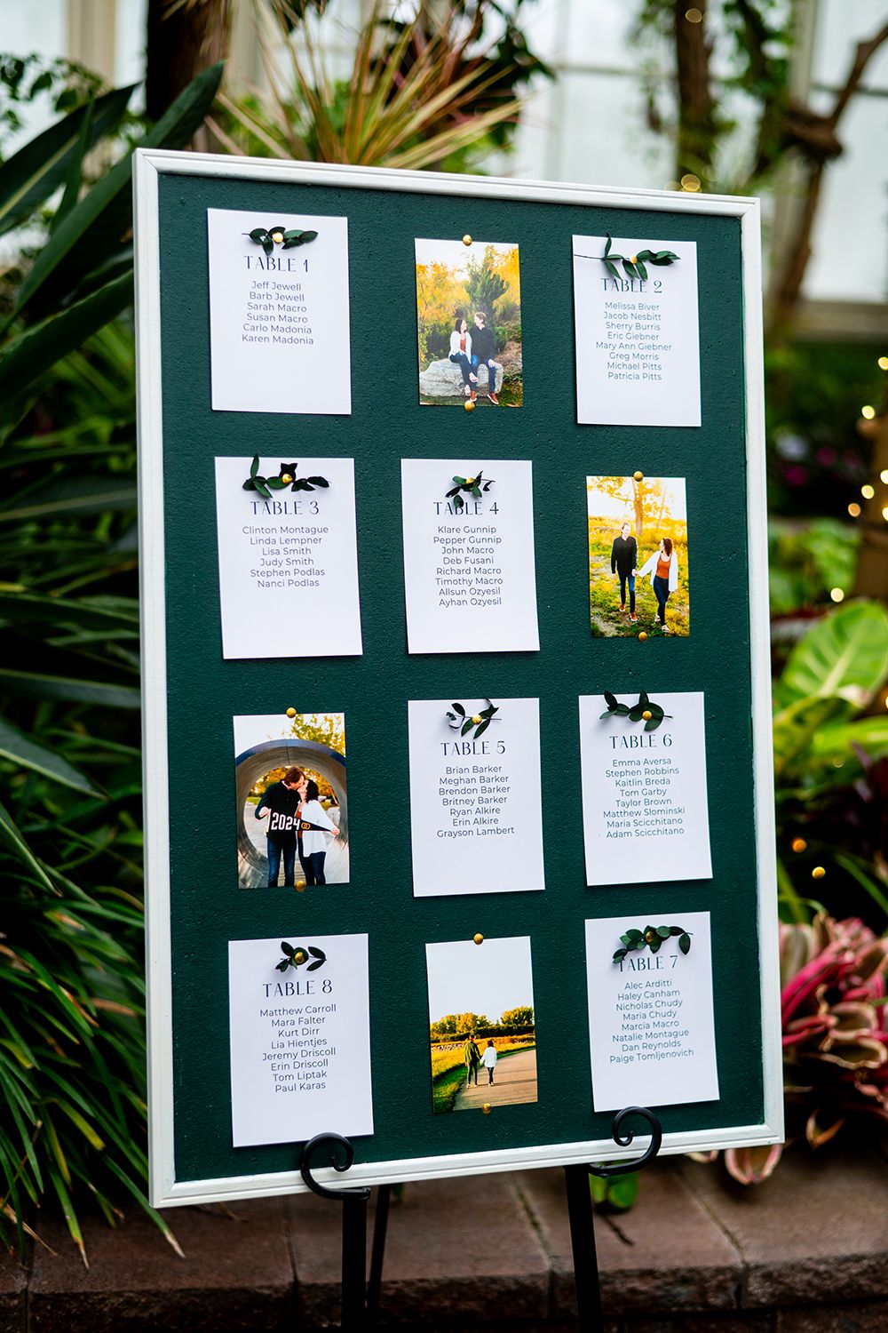 A green wedding seating chart display board with photos and text arranged in a grid pattern.