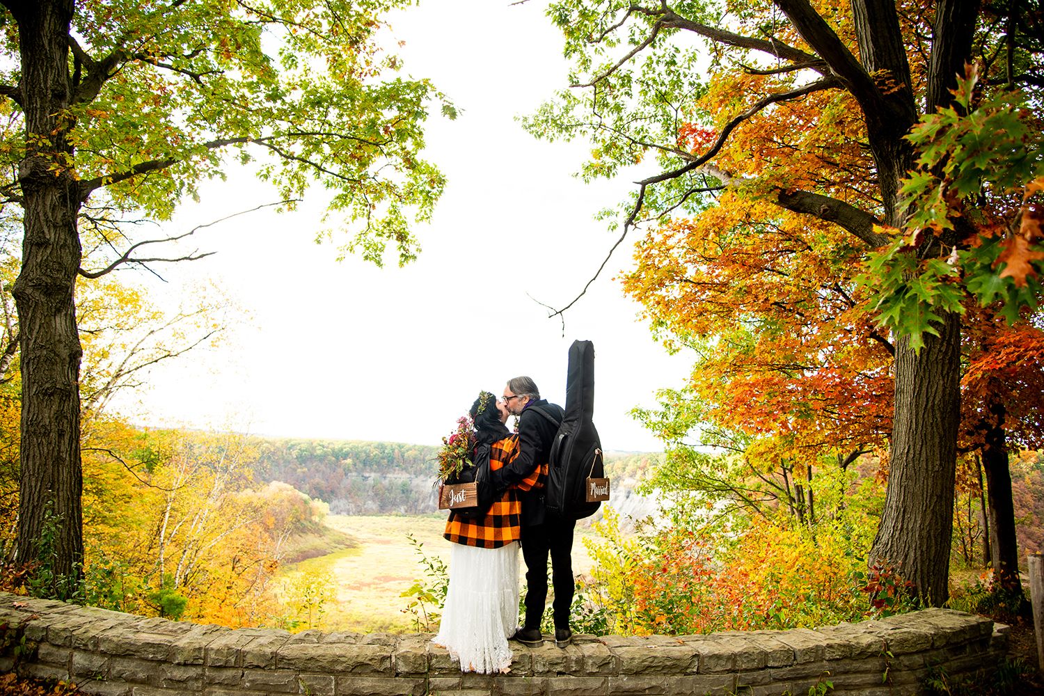 A couple enjoys a scenic autumn view from a stone overlook surrounded by colorful fall trees.