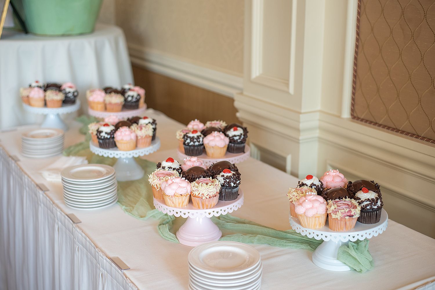 Display of chocolate and pink frosted cupcakes arranged on white cake stands at a wedding dessert table.