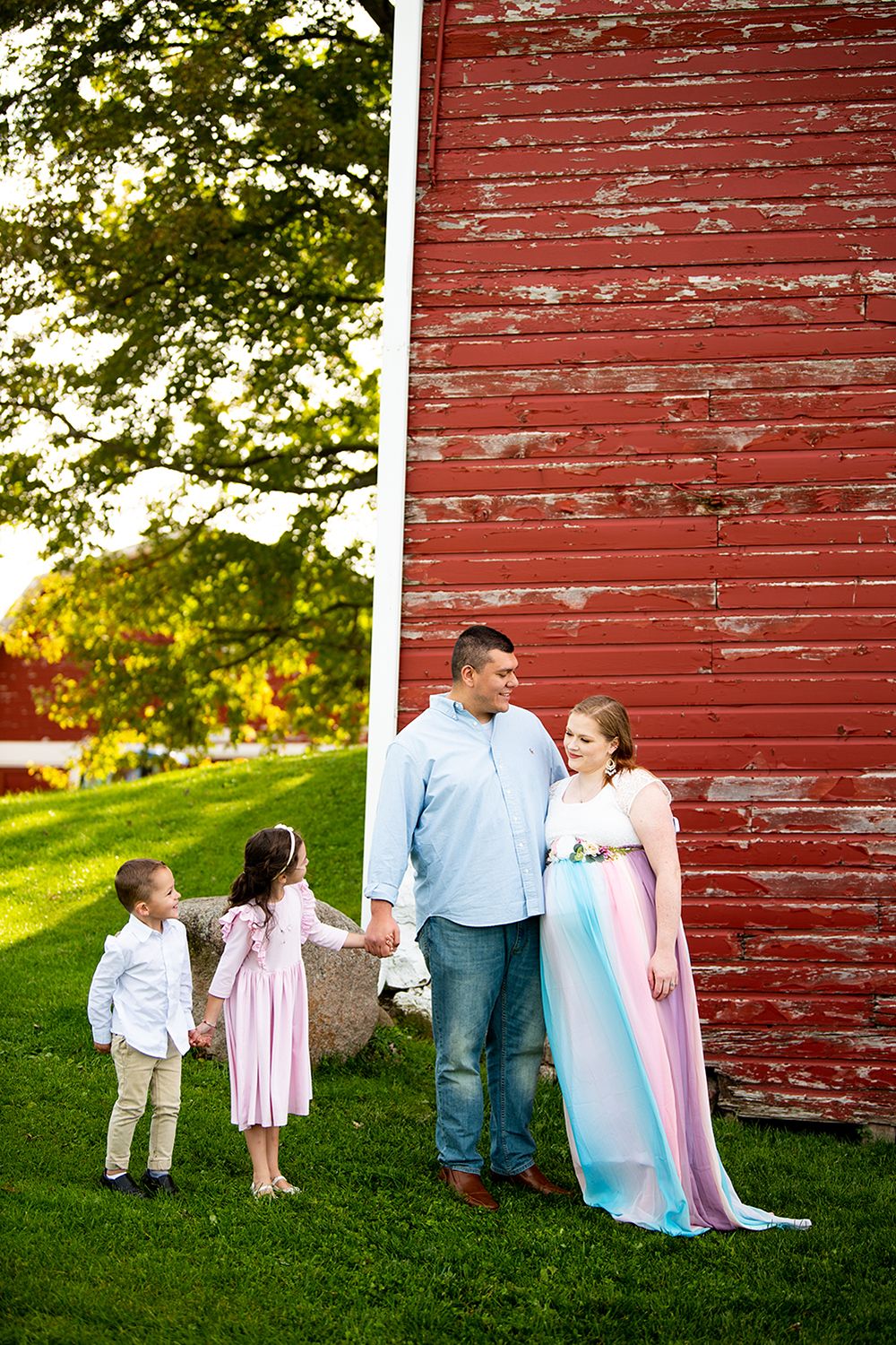 A sweet interaction in front of a rustic red barn wall during a sunny golden hour photo session.