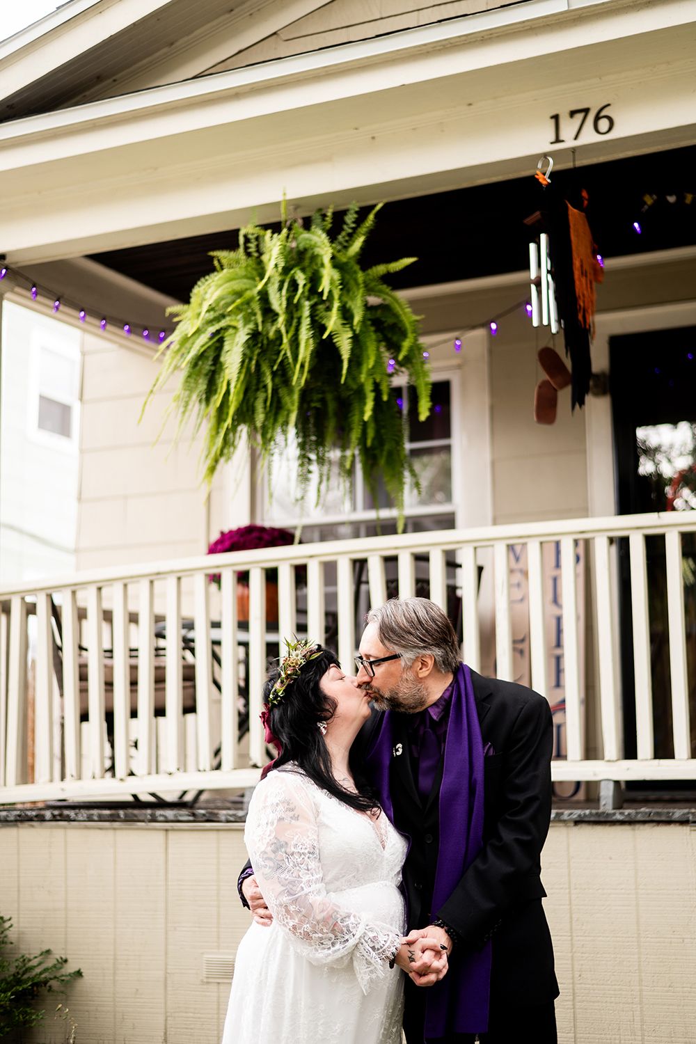 A couple shares intimate moments on a porch decorated with hanging plants and white railings.