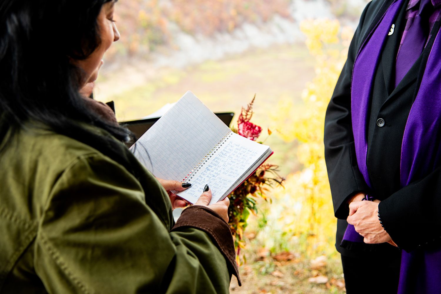 Student writing or journaling outdoors on a sunny autumn day while wearing a purple and olive green coat.