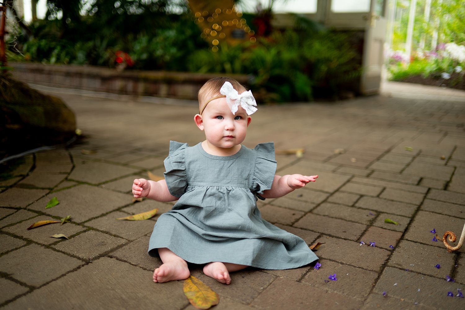 Small figure in gray dress seated on stone patio with autumn leaves scattered around.