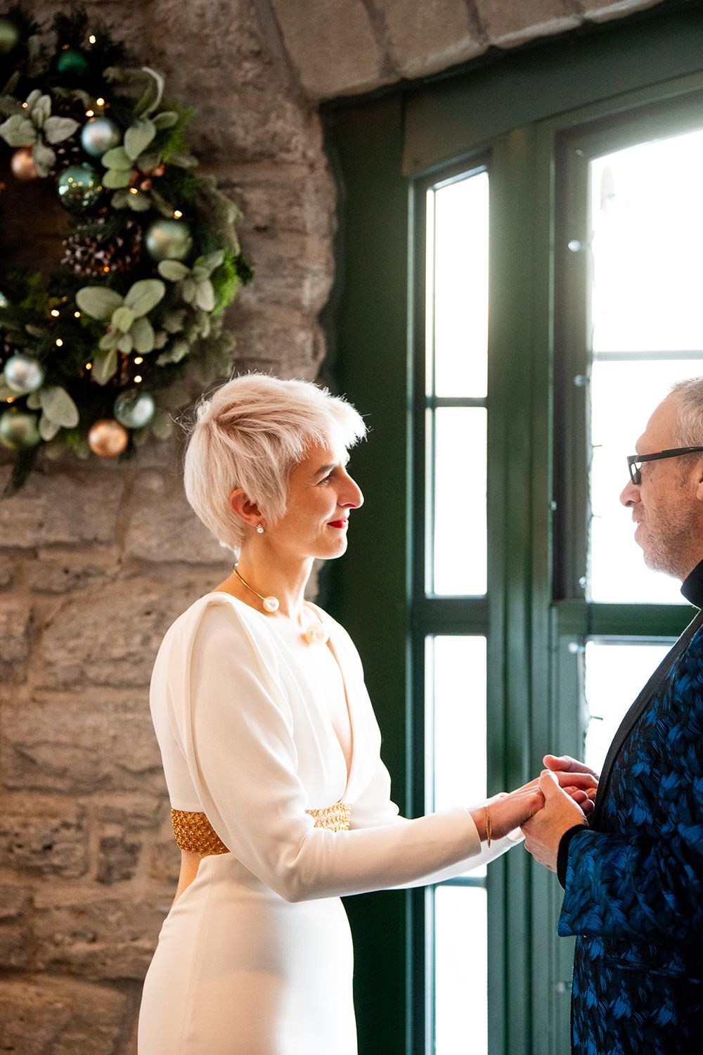 Guests enjoying an intimate moment of laughter together during a wintery indoor celebration near stone walls and wreaths.