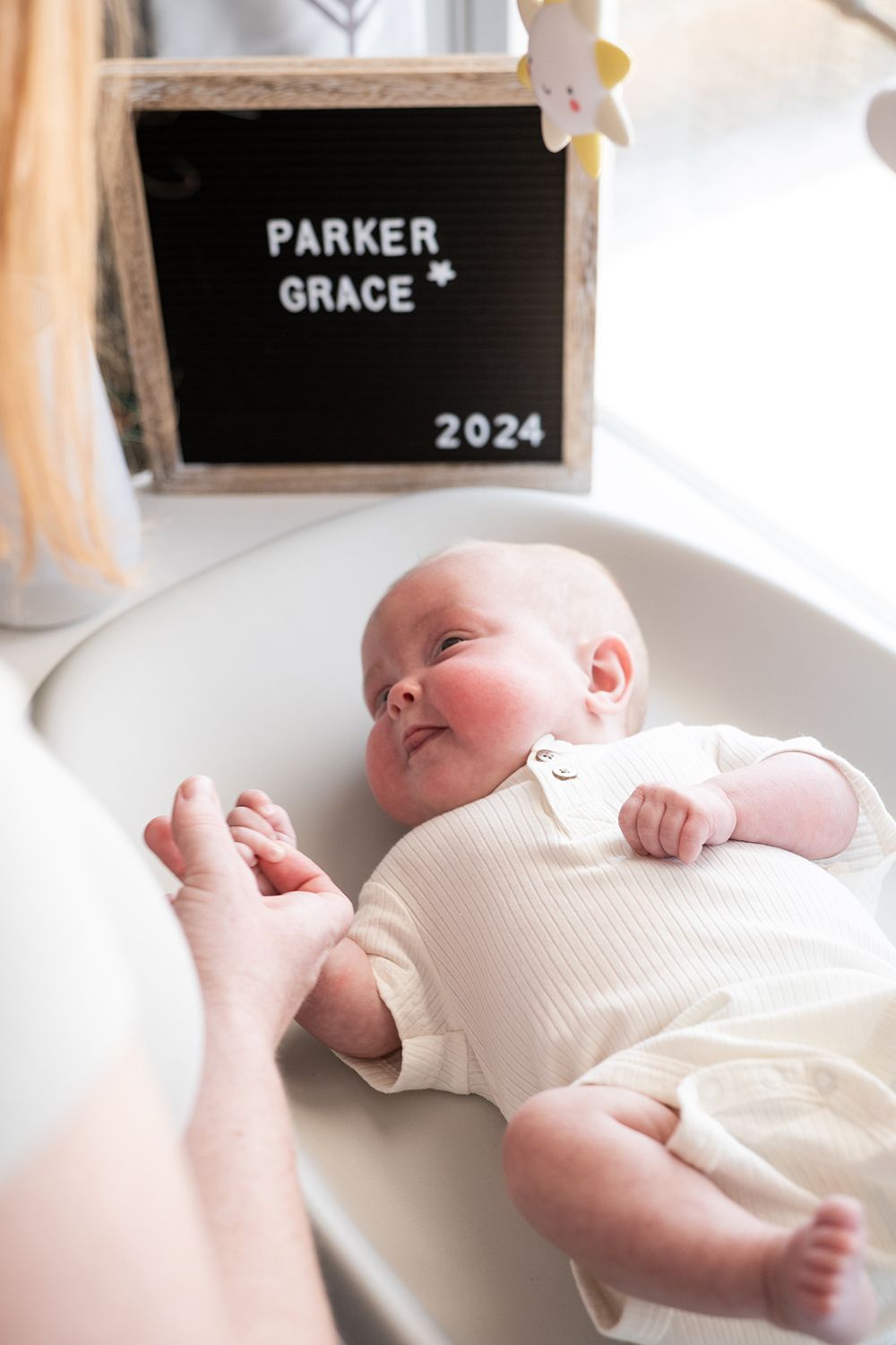 A baby in white clothing lying on a white changing pad with a black letterboard visible in the frame.
