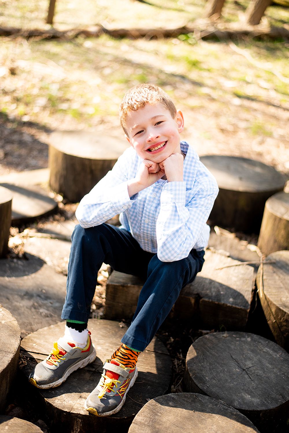 Casual outdoor portrait sitting on wooden logs in sunlit forest setting.
