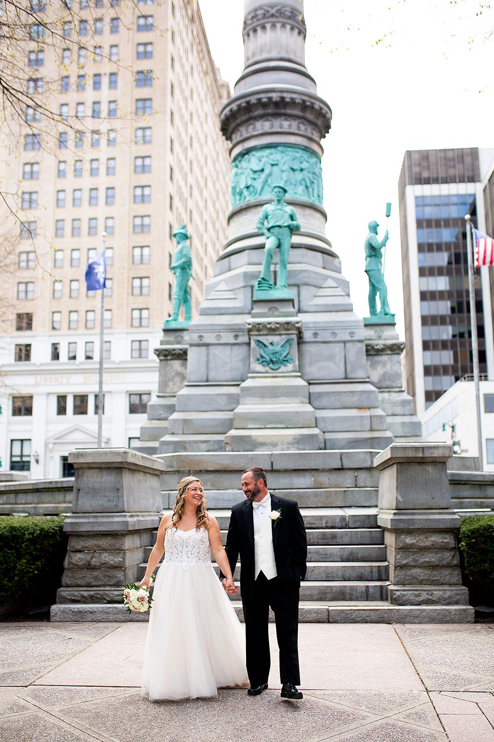 A series of wedding portraits showing a couple walking along ornate stone pillars topped with turquoise statues in an urban setting.