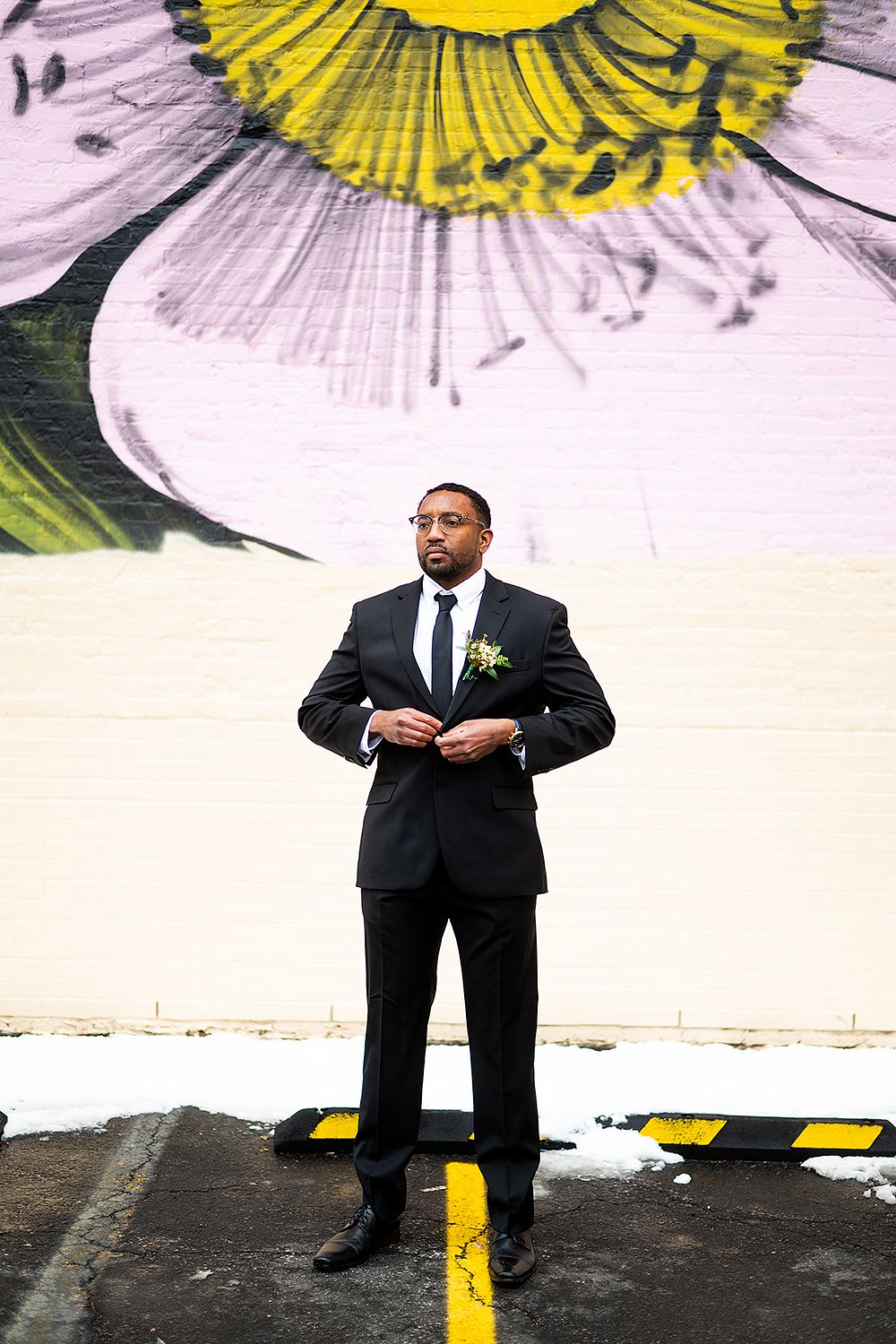 Formal portrait against a large floral mural with yellow and white daisy design in urban setting.