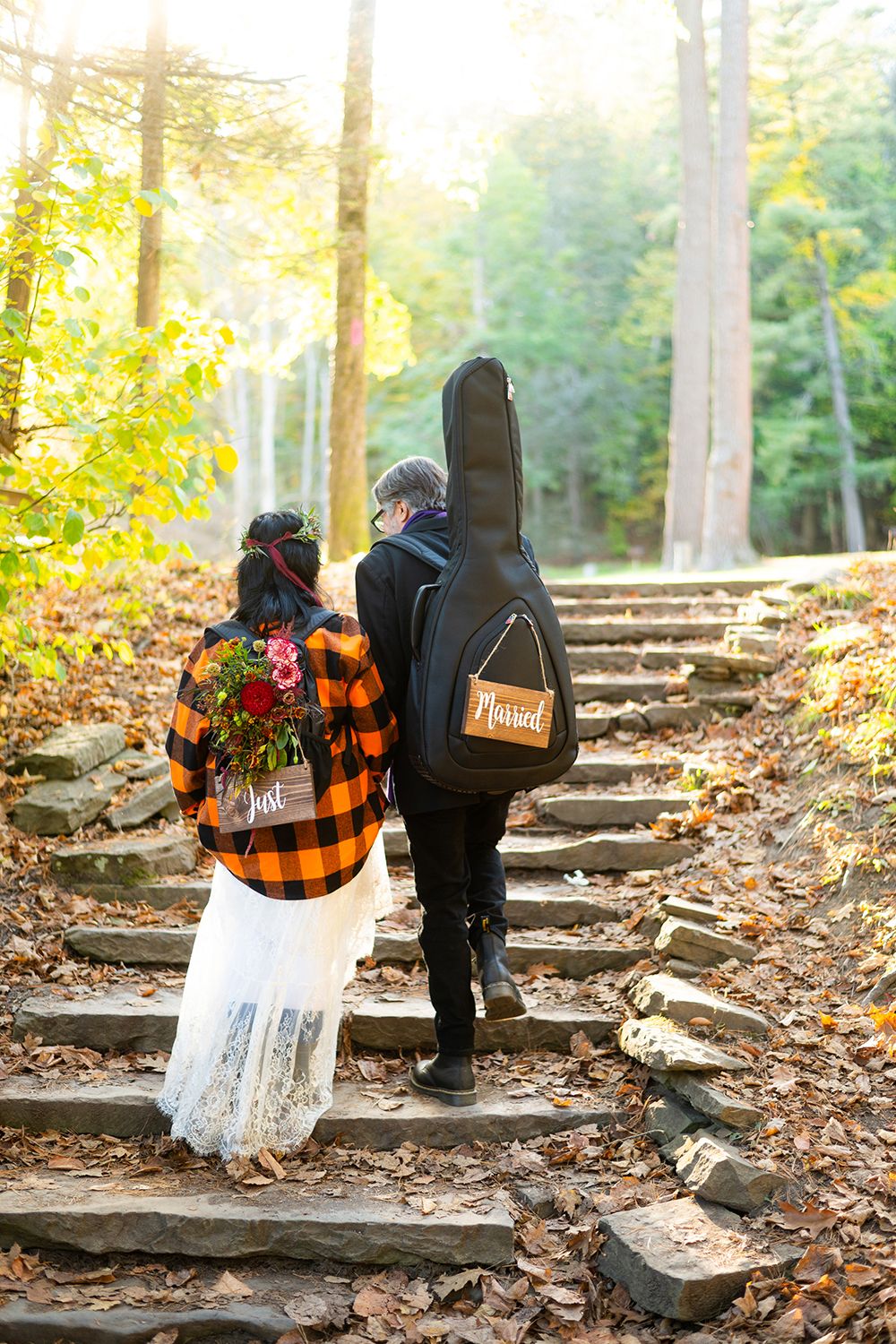 A guitar case and lace dress sit on stone steps in a forest during autumn.